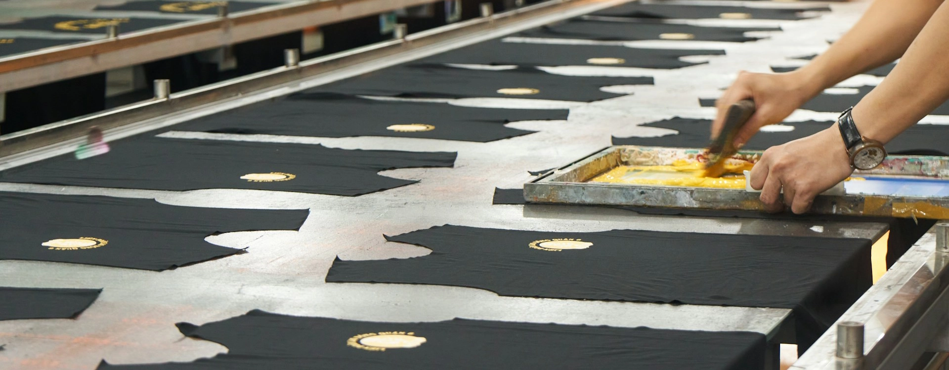 Produzione serigrafica su larga scala di magliette nere con stampa gialla applicata manualmente tramite racla