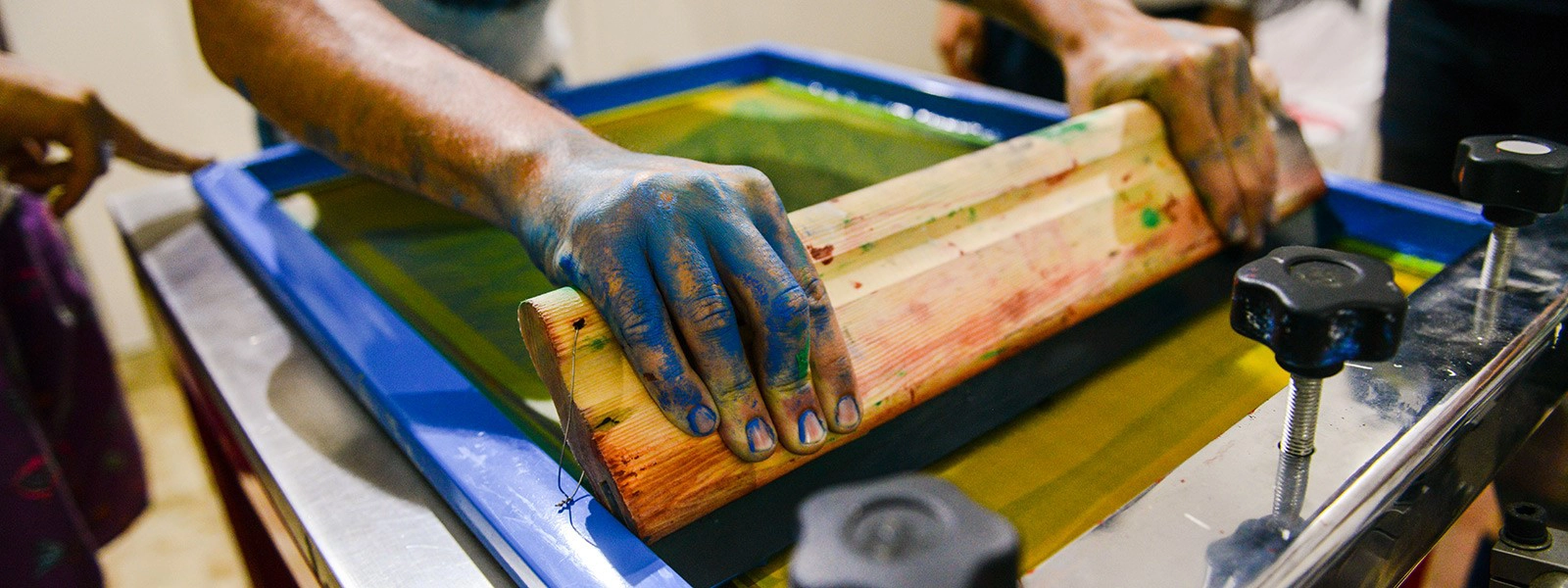 Operatore durante la stampa serigrafica manuale su tessuto con telaio e racla in legno