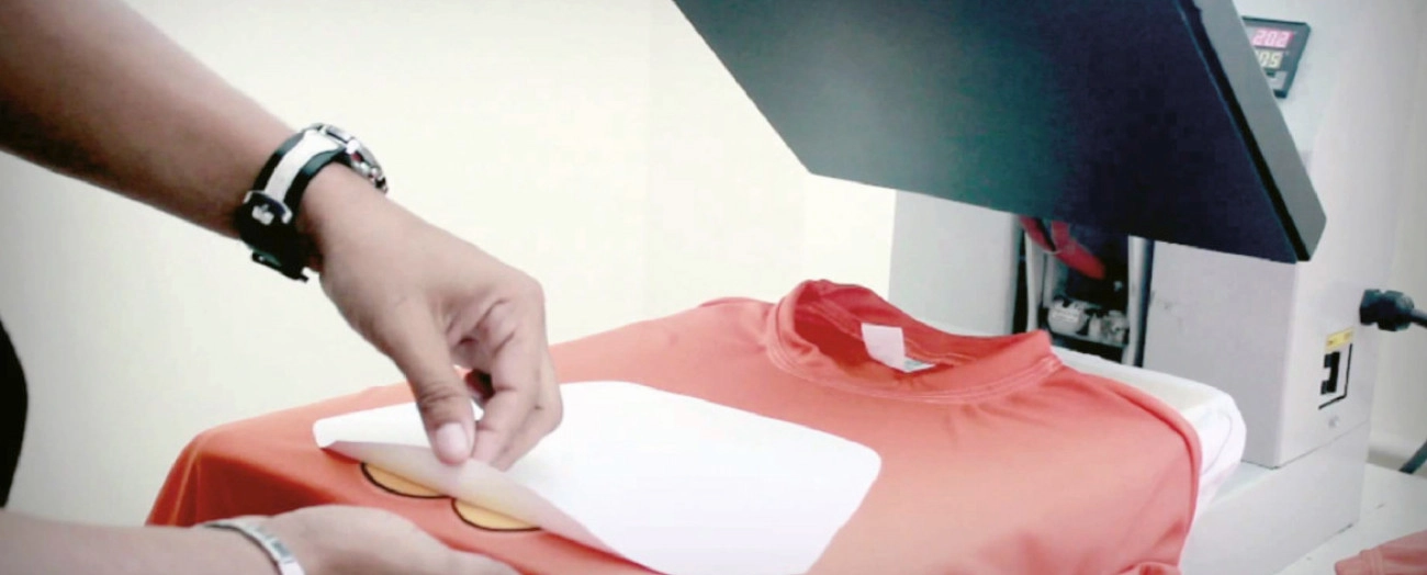 Operatore rimuove la pellicola transfer dopo la pressatura a caldo di un design su maglietta arancione